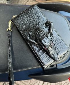 Chiếc ví cầm tay nam da cá sấu nguyên con trên xe, thể hiện sự sang trọng và tiện dụng khi sử dụng hàng ngày.