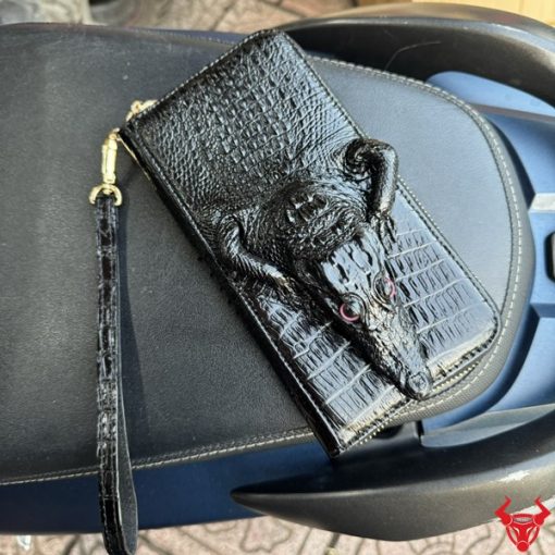 Chiếc ví cầm tay nam da cá sấu nguyên con trên xe, thể hiện sự sang trọng và tiện dụng khi sử dụng hàng ngày.