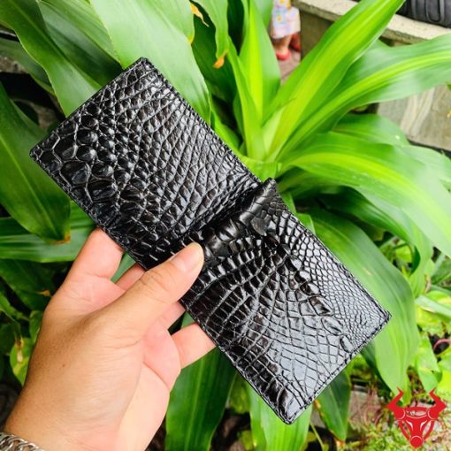 Hình ảnh ví kẹp tiền da cá sấu đen VOA5, phong cách thời trang, được cầm trên tay giữa cảnh lá xanh tươi.
