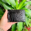 Hình ảnh ví kẹp tiền da cá sấu gai tay màu đen VOA5, thiết kế thời trang, sang trọng, cầm trên tay trước nền lá xanh.