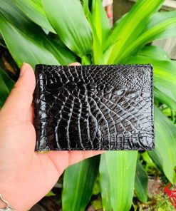 Hình ảnh ví kẹp tiền da cá sấu gai tay màu đen VOA5, thiết kế thời trang, sang trọng, cầm trên tay trước nền lá xanh.