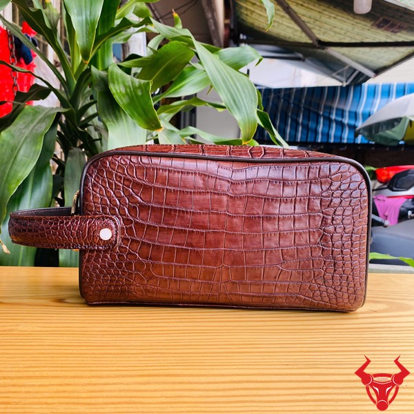 Một chiếc túi clutch hộp da cá sấu màu nâu đất, thể hiện phong cách thời trang cao cấp và đẳng cấp cổ điển.