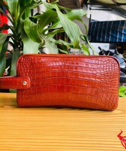 Một chiếc túi clutch da cá sấu đỏ, thể hiện phong cách thời trang sang trọng và gọn gàng.