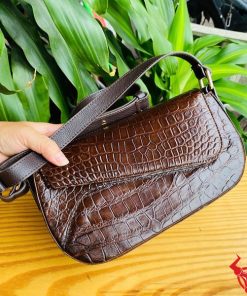 Hình ảnh túi đeo vai da cá sấu HM-20 màu nâu, đặt trên bàn gỗ, nổi bật giữa cây xanh với phong cách thời trang.