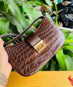 Hình ảnh túi đeo vai da bụng cá sấu HM-19 màu nâu, khóa vàng, đặt trên giá gỗ, thể hiện phong cách sang trọng và cá tính.