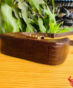 Hình ảnh túi đeo vai da bụng cá sấu HM-19 màu nâu, khóa vàng, đặt trên giá gỗ, thể hiện phong cách sang trọng và cá tính.