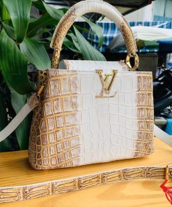 Hình ảnh túi xách nữ da cá sấu bạch tạng nhũ vàng, đặt trên bàn gỗ, nổi bật với phong cách sang trọng và đẳng cấp.