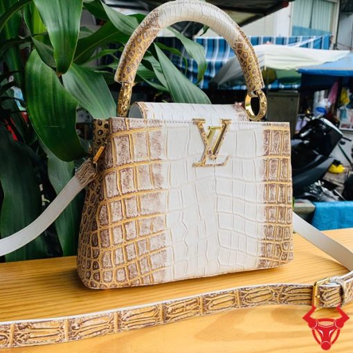 Hình ảnh túi xách nữ da cá sấu bạch tạng nhũ vàng, đặt trên bàn gỗ, nổi bật với phong cách sang trọng và đẳng cấp.