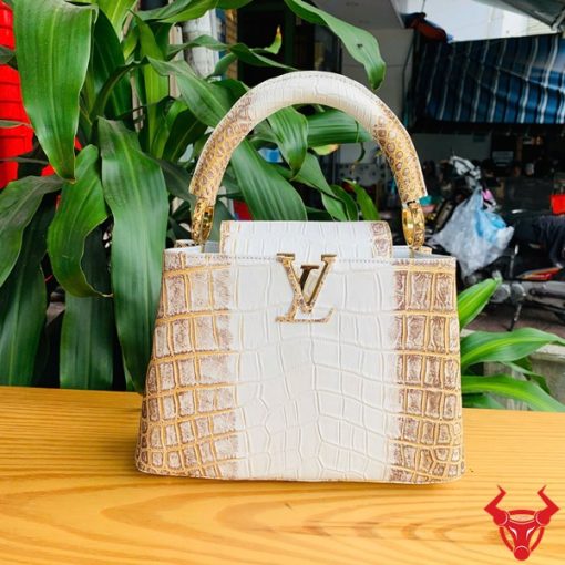 Hình ảnh túi xách da cá sấu bạch tạng nhũ vàng, đặt trên bàn gỗ, thể hiện sự sang trọng và quý phái.