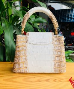 Hình ảnh túi xách da cá sấu bạch tạng nhũ vàng, đặt trên bàn gỗ, nổi bật với phong cách quý phái và đẳng cấp.