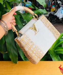 Hình ảnh túi xách da cá sấu bạch tạng nhũ vàng, đặt trên bàn gỗ, thể hiện sự sang trọng và thời trang.