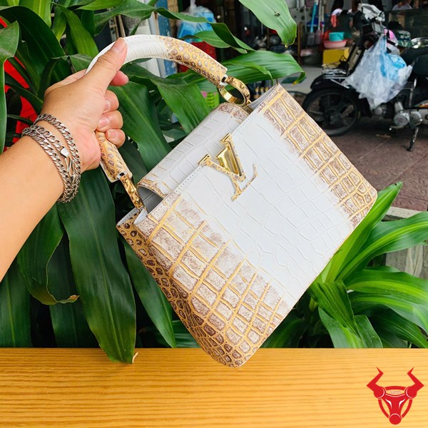Quý Phái Với Túi Xách Da Cá Sấu Nhũ Vàng Hình ảnh túi xách da cá sấu bạch tạng nhũ vàng, đặt trên bàn gỗ, thể hiện sự sang trọng và thời trang.