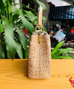 Hình ảnh túi xách da cá sấu bạch tạng nhũ vàng, đặt trên bàn gỗ, nổi bật với phong cách quý phái và đẳng cấp.
