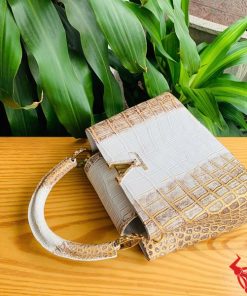 Hình ảnh túi xách da cá sấu bạch tạng nhũ vàng, đặt trên bàn gỗ, thể hiện phong cách thời trang đẳng cấp.