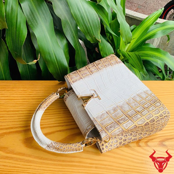 Túi Xách Nữ TN - Thời Trang Đỉnh Cao Hình ảnh túi xách da cá sấu bạch tạng nhũ vàng, đặt trên bàn gỗ, thể hiện phong cách thời trang đẳng cấp.