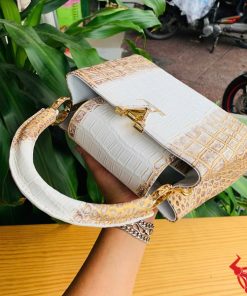 Hình ảnh túi xách da cá sấu bạch tạng nhũ vàng, đặt trên bàn gỗ, nổi bật với sự sang trọng và quý phái.