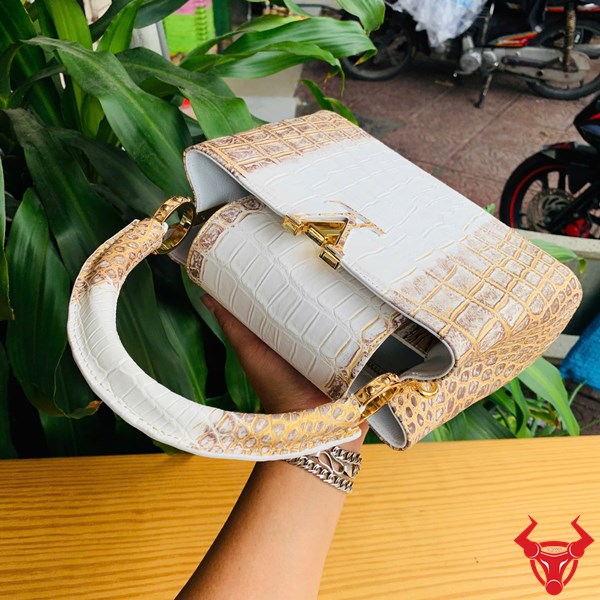 Phong Cách Quý Phái Với Túi Da Cá Sấu Nhũ Vàng Hình ảnh túi xách da cá sấu bạch tạng nhũ vàng, đặt trên bàn gỗ, nổi bật với sự sang trọng và quý phái.
