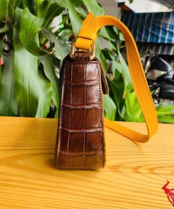 Hình ảnh túi xách da bụng cá sấu HM-18, nâu vàng viền da bò, đặt trên giá gỗ, nổi bật với phong cách sang trọng.