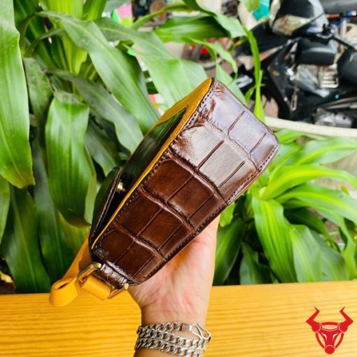 Hình ảnh túi xách da bụng cá sấu HM-18, nâu vàng viền da bò, đặt trên giá gỗ, thể hiện phong cách sang trọng.