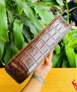 Hình ảnh túi xách da bụng cá sấu HM-18, nâu vàng viền da bò, đặt trên giá gỗ, nổi bật giữa cây xanh với phong cách thời trang.