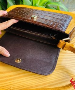 Hình ảnh túi xách da bụng cá sấu HM-18, nâu vàng viền da bò, đặt trên giá gỗ, thể hiện phong cách sang trọng.