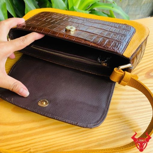 Hình ảnh túi xách da bụng cá sấu HM-18, nâu vàng viền da bò, đặt trên giá gỗ, thể hiện phong cách sang trọng.