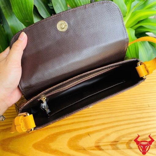 Hình ảnh túi xách da bụng cá sấu HM-18, nâu vàng viền da bò, đặt trên giá gỗ, nổi bật với phong cách thời trang sang trọng.