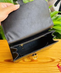 Hình ảnh túi xách HM-23 da cá sấu màu đen, thiết kế sang trọng, khóa vàng lấp lánh, trên bàn gỗ với lá xanh và xe máy phía sau.