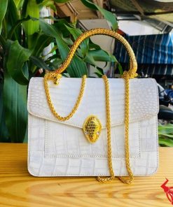 Hình ảnh túi xách da cá sấu bạch tạng HM-16, quai vàng rắn, đặt trên bàn gỗ, thể hiện phong cách sang trọng và cá tính.