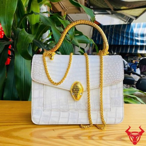 Hình ảnh túi xách da cá sấu bạch tạng HM-16, quai vàng rắn, đặt trên bàn gỗ, thể hiện phong cách sang trọng và cá tính.