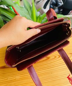 Hình ảnh túi xách da cá sấu HM-21 màu nâu đỏ, kiểu dáng cao cấp, khóa vàng, đặt trên bàn gỗ với lá xanh và xe máy mờ phía sau.