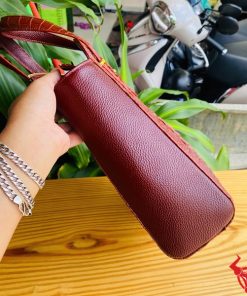 Hình ảnh túi xách HM-21 da cá sấu màu nâu đỏ, thiết kế cao cấp, khóa vàng nổi bật, trên bàn gỗ với lá xanh và xe máy phía sau.