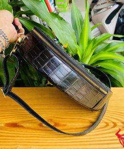 Hình ảnh túi xách HM-22 da cá sấu hình trái tim màu đen, thiết kế quý phái, khóa vàng, trên giá gỗ với lá xanh và xe máy phía sau.