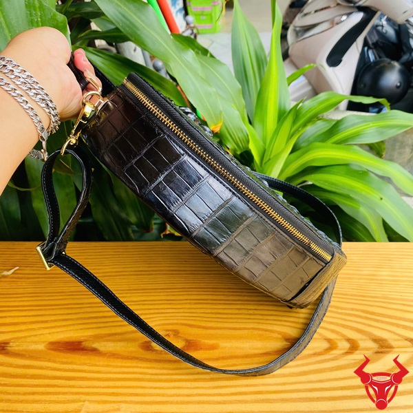 Quý phái hiện đại cùng HM-22 túi xách hình trái tim Hình ảnh túi xách HM-22 da cá sấu hình trái tim màu đen, thiết kế quý phái, khóa vàng, trên giá gỗ với lá xanh và xe máy phía sau.