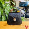 Hình ảnh túi xách da cá sấu trơn bụng HM-24 màu đen, thiết kế quý phái, khóa vàng, đặt trên bàn gỗ với nền lá xanh và xe máy mờ phía sau.