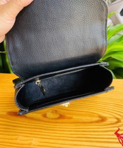 Hình ảnh túi xách HM-24 da cá sấu màu đen, thiết kế thanh lịch, khóa vàng nổi bật, trên bàn gỗ với lá xanh và xe máy phía sau.
