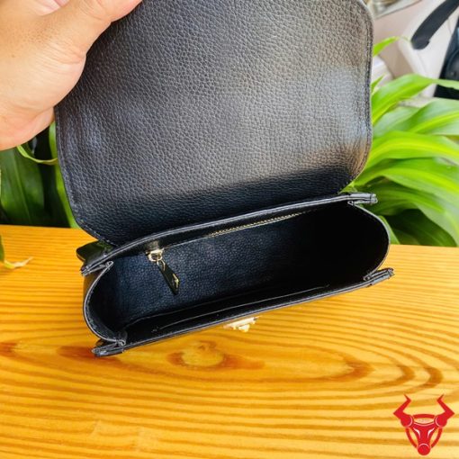 Hình ảnh túi xách HM-24 da cá sấu màu đen, thiết kế thanh lịch, khóa vàng nổi bật, trên bàn gỗ với lá xanh và xe máy phía sau.