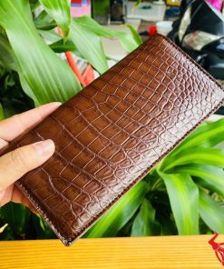 Cận cảnh ví cầm tay nâu đất bằng da cá sấu thật, bề mặt vân đẹp.