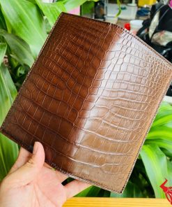 Ví da bụng cá sấu nâu dạng đứng gập đôi cầm bởi tay nam giới.