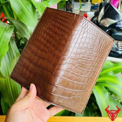 Ví da bụng cá sấu nâu dạng đứng gập đôi cầm bởi tay nam giới.