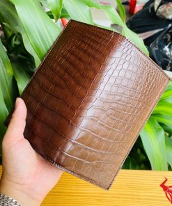Ví nâu da cá sấu kiểu đứng hai gấp trong tay người đeo vòng bạc.