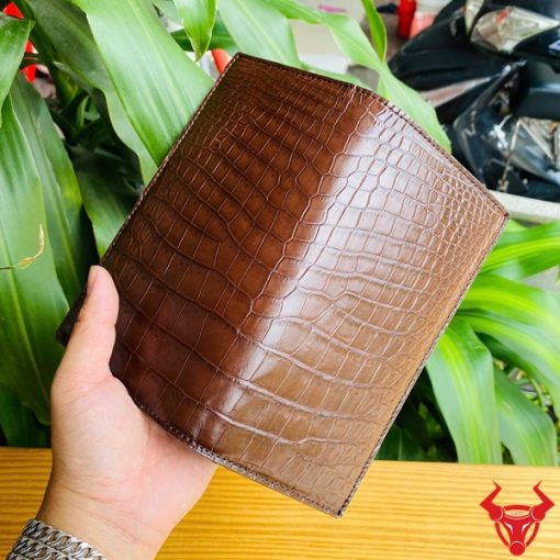 Ví nâu da cá sấu kiểu đứng hai gấp trong tay người đeo vòng bạc.