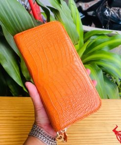 Cận cảnh ví cam da cá sấu thật cầm bởi tay đeo vòng bạc.