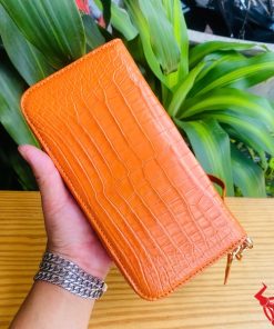 Ví cầm tay màu cam nổi bật, đường vân cá sấu tinh tế.