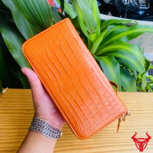 Ví cầm tay màu cam nổi bật, đường vân cá sấu tinh tế.