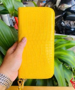 Ví da cá sấu bụng màu vàng sang trọng được cầm trên tay.