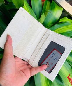 Ví đứng màu trắng viền đen nổi bật được cầm trên nền lá cây.
