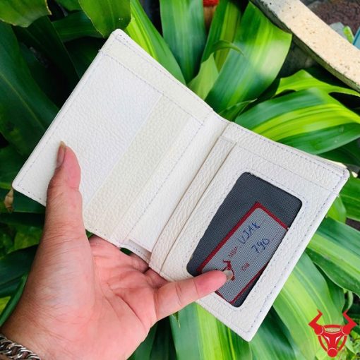 Ví đứng màu trắng viền đen nổi bật được cầm trên nền lá cây.