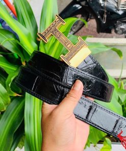 Hình ảnh thắt lưng TSK103 màu đen, da cá sấu cao cấp, đầu khóa ray thép không gỉ, cầm trên tay với cây xanh phía sau.