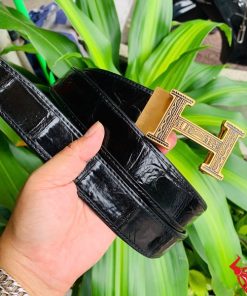 Hình ảnh thắt lưng TSK103 màu đen, da cá sấu sang trọng, đầu khóa ray thép không gỉ, cầm trên tay với nền cây xanh và mô tô.